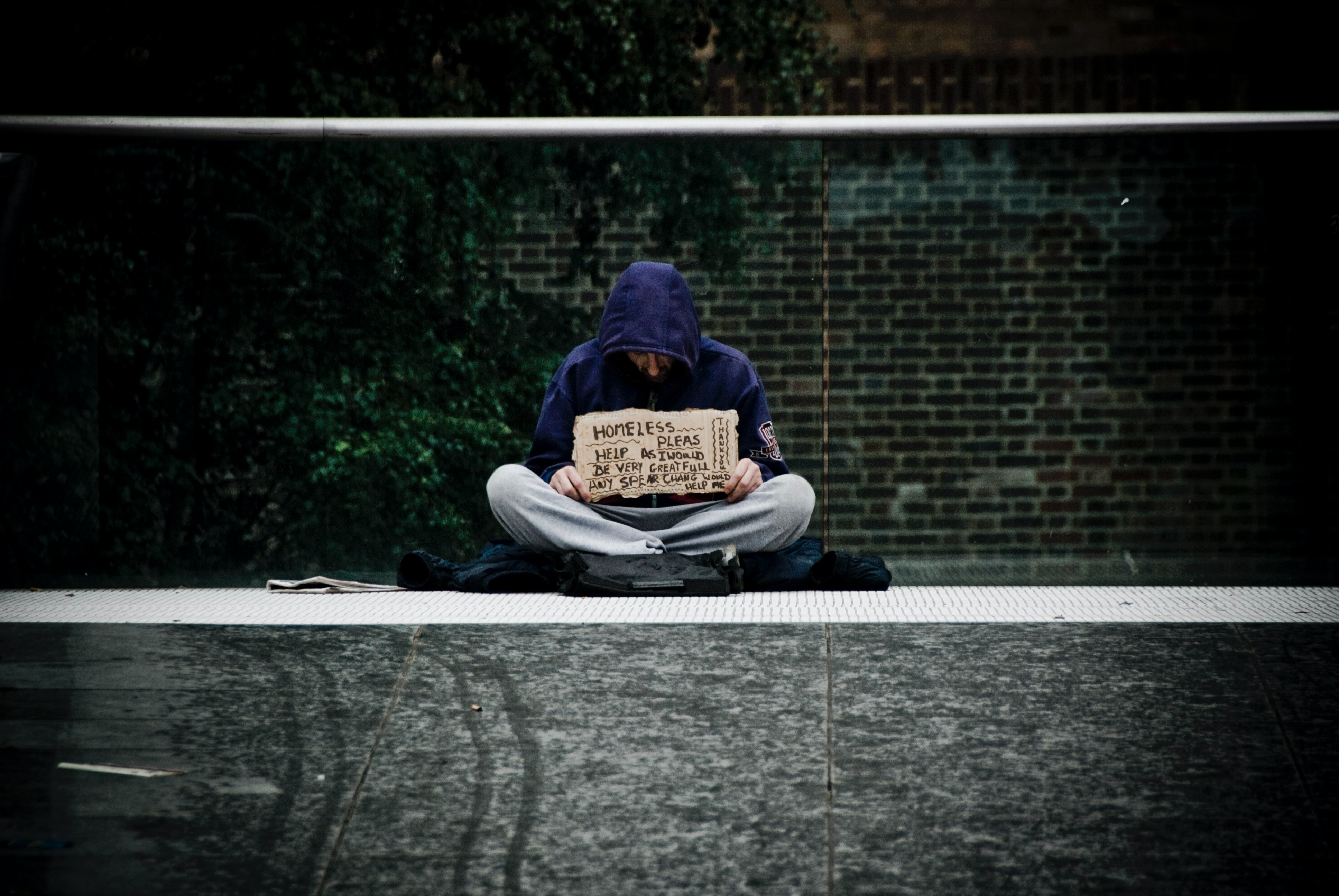 A homeless person sitting on the street with a sign asking for help